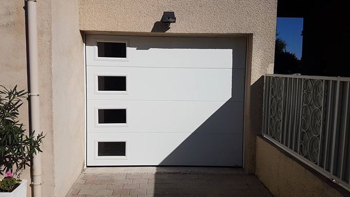 Après les travaux : porte de garage sectionnelle blanche à hublots rectangulaires posée à la place de l'ancienne basculante