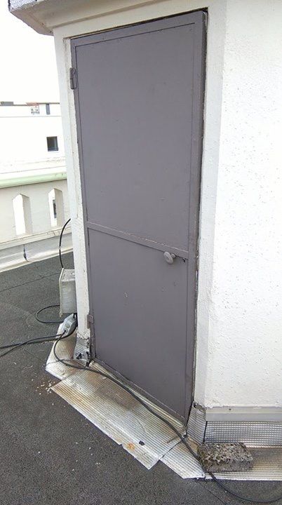 Avant les travaux : ancienne porte métallique grise d'un accès en toit-terrasse