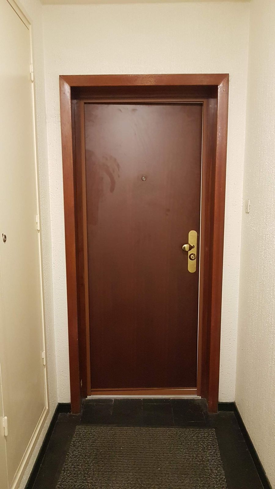 Porte palière pleine ton acajou avec serrure de sécurité et habillage bois, dans un couloir d'immeuble
