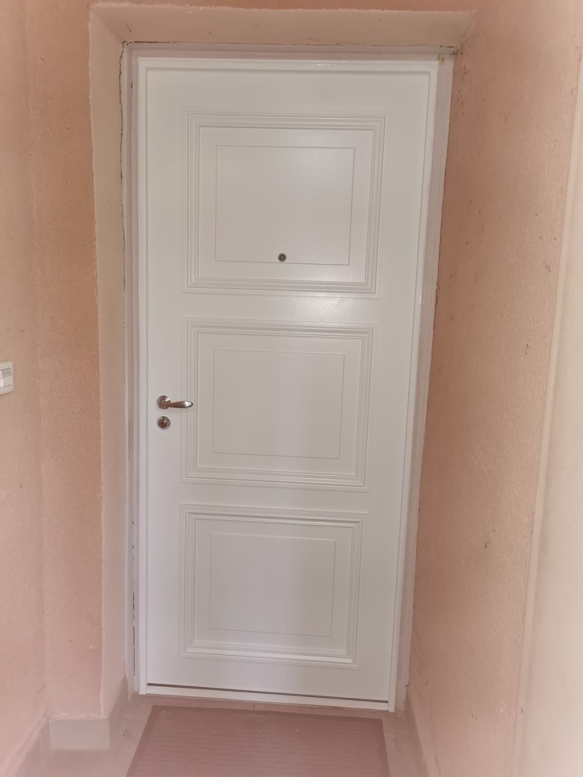 Porte blindée blanche à trois panneaux moulurés, posée sur un palier d'immeuble