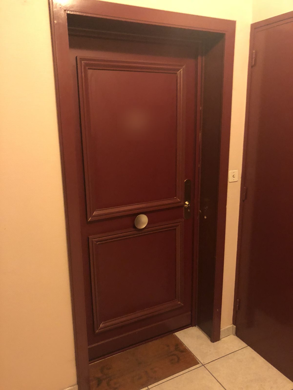 Porte d'entrée blindée bordeaux à moulures posée sur un palier d'immeuble