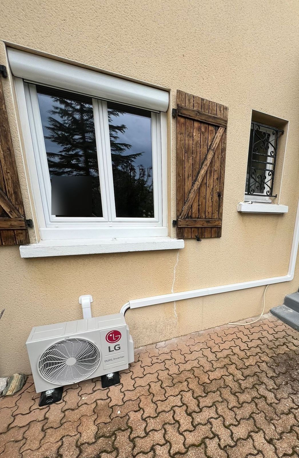 Unité extérieure de climatisation posée au sol sur supports, liaisons protégées par une goulotte blanche
