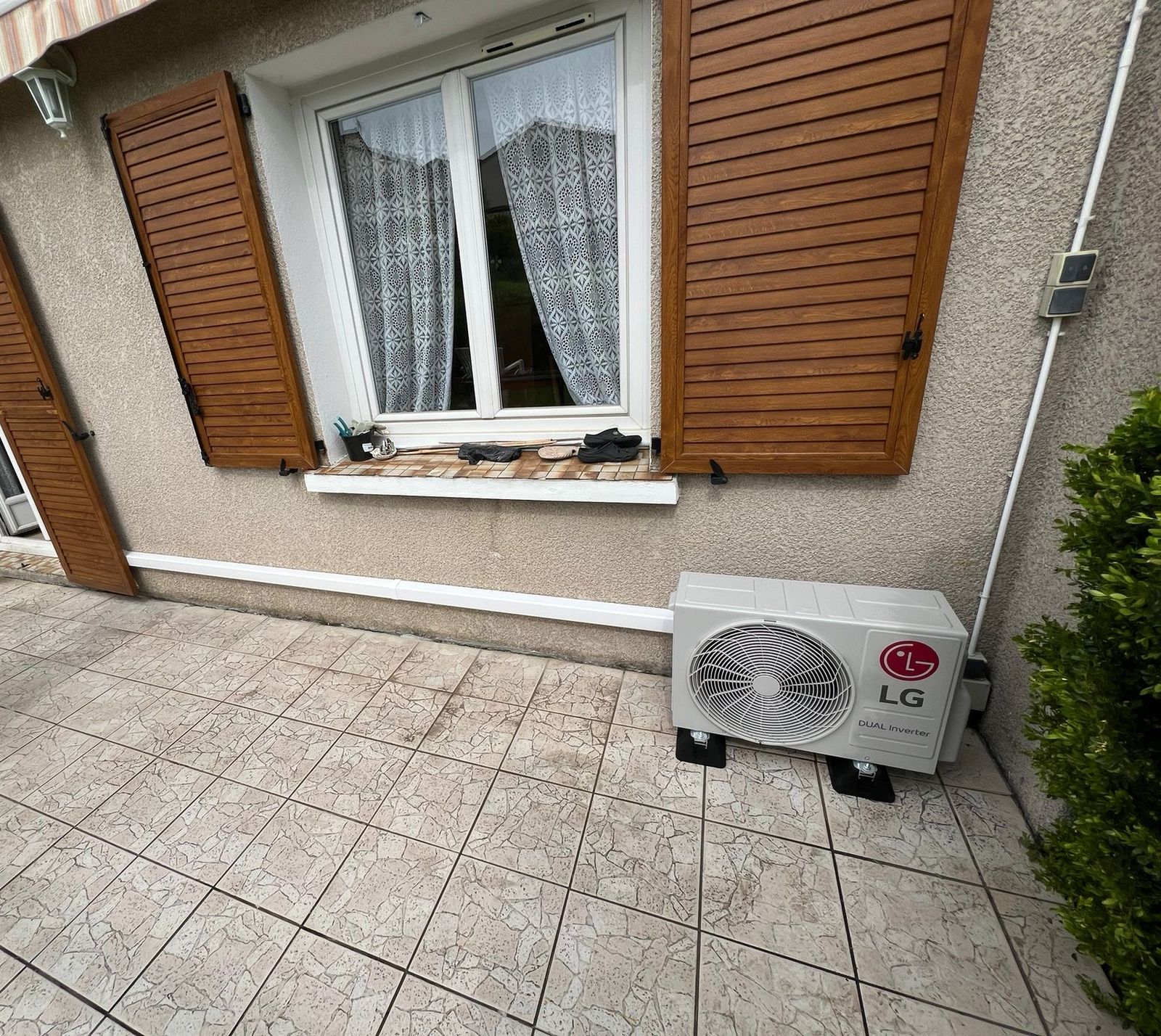 Unité extérieure de climatisation posée sur une terrasse au pied d'une façade, avec goulotte blanche