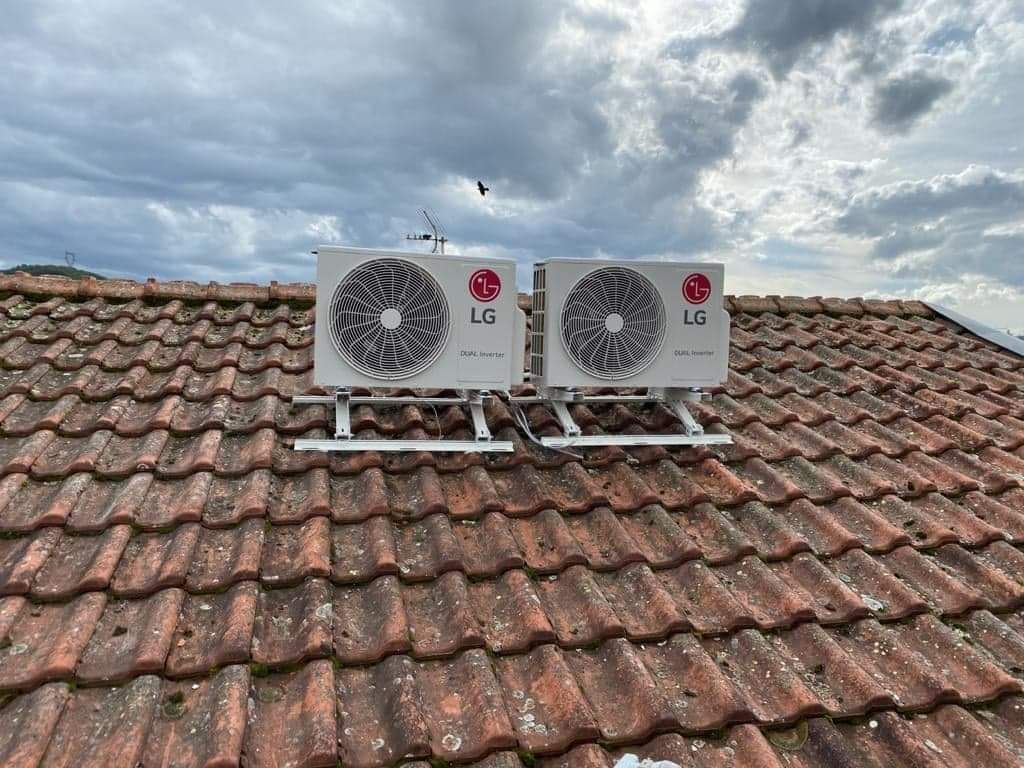 Deux unités extérieures de climatisation posées sur des supports sur un toit en tuiles, sous un ciel nuageux