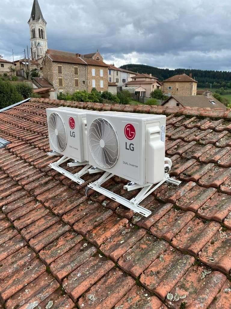 Deux unités extérieures de climatisation installées sur un toit en tuiles, avec un village et son clocher en arrière-plan