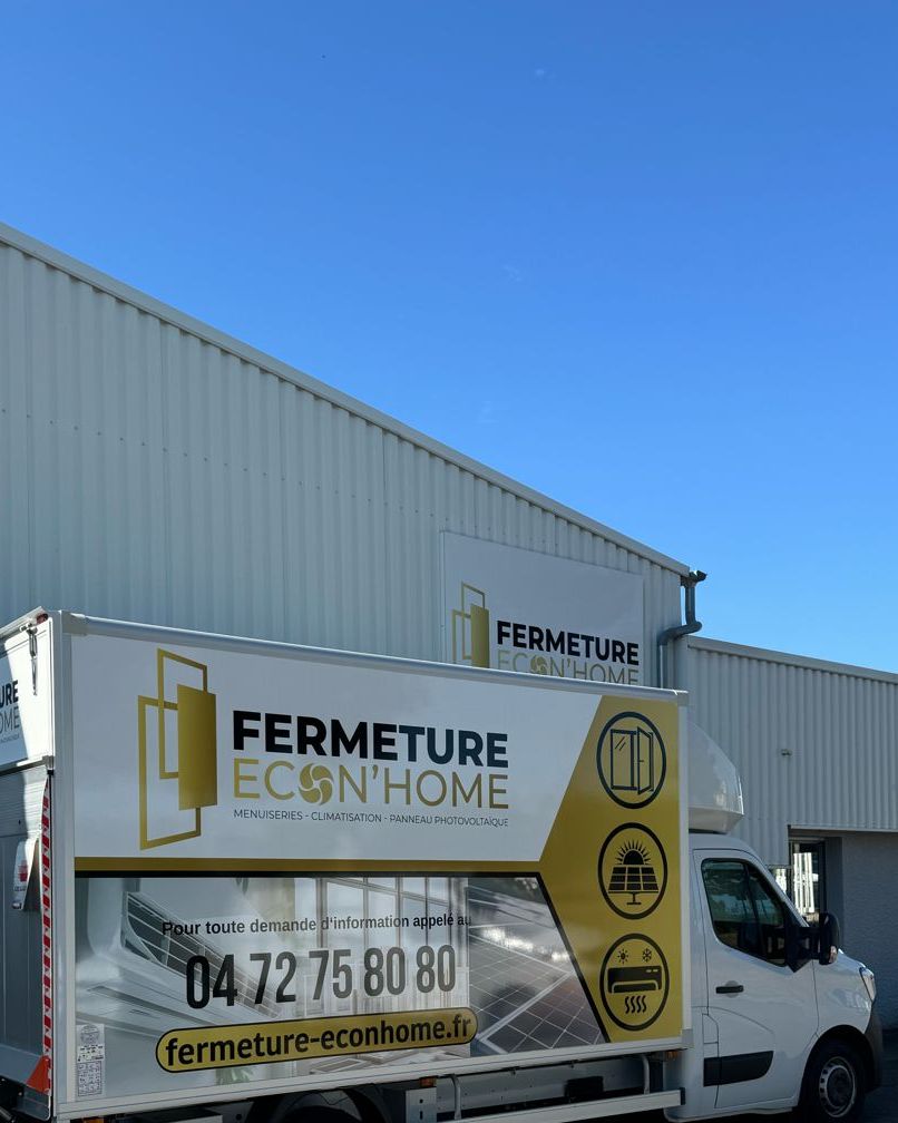 Camion floqué Fermeture Econ'Home, aux couleurs or et blanc, stationné devant un bâtiment à l'enseigne de l'entreprise sous un ciel bleu