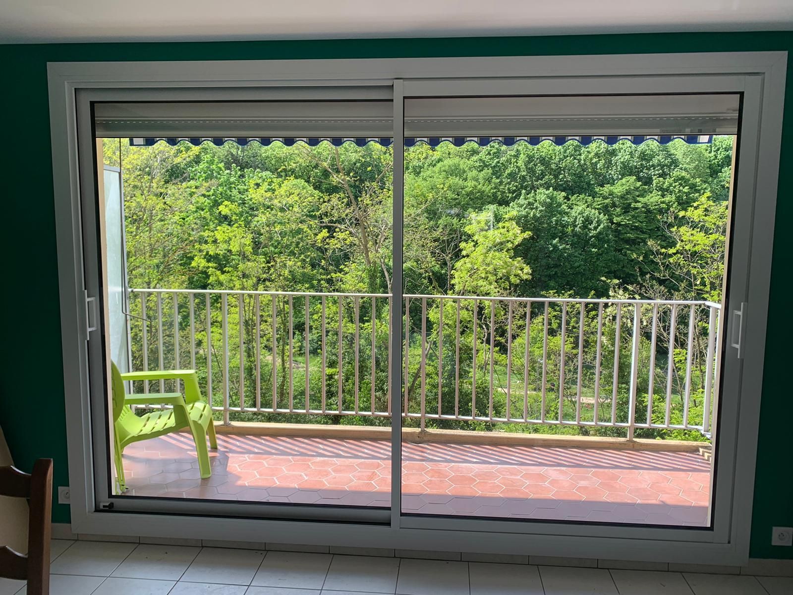 Grande baie coulissante blanche ouvrant sur un balcon face aux arbres