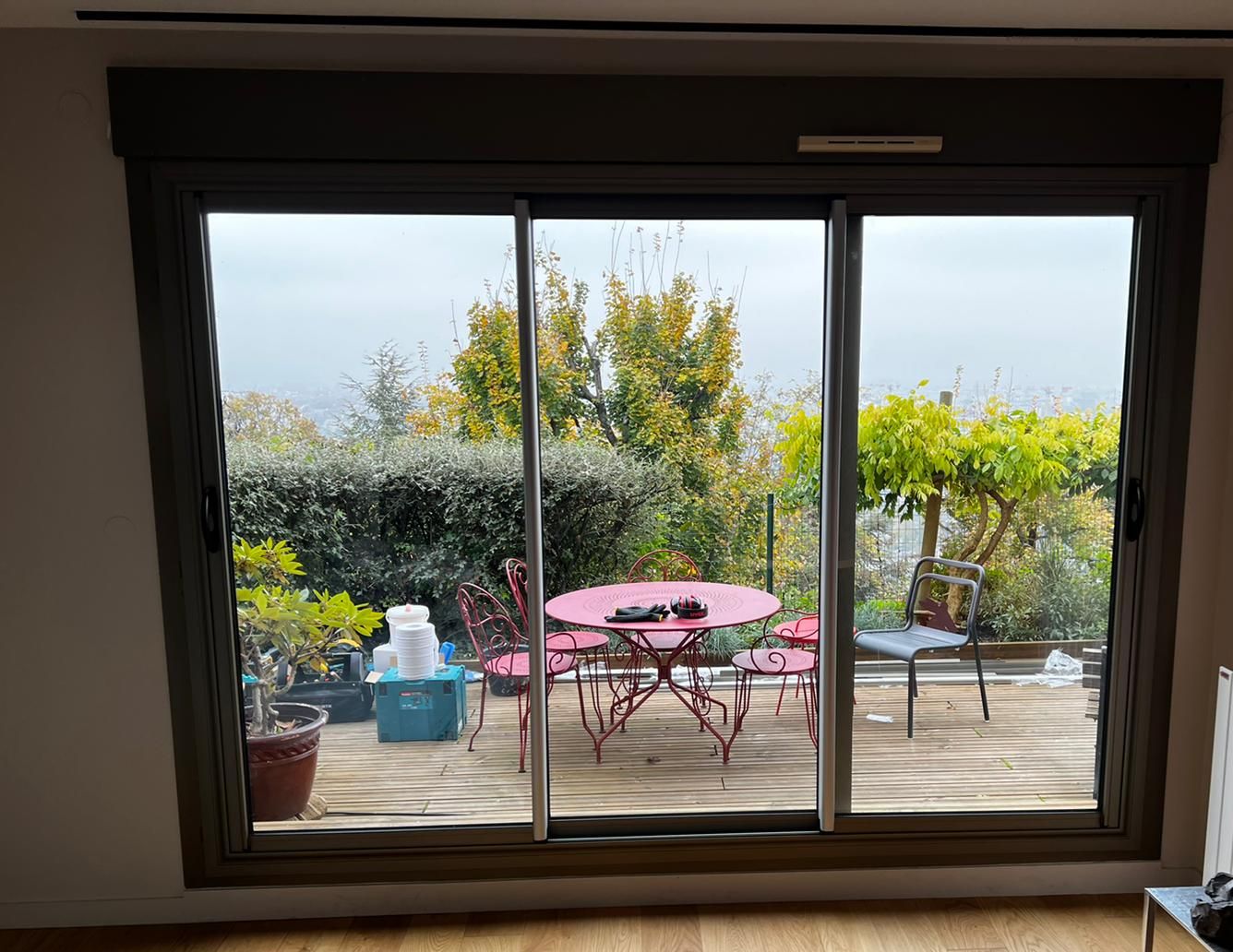 Baie coulissante gris anthracite à trois vantaux ouvrant sur une terrasse en bois