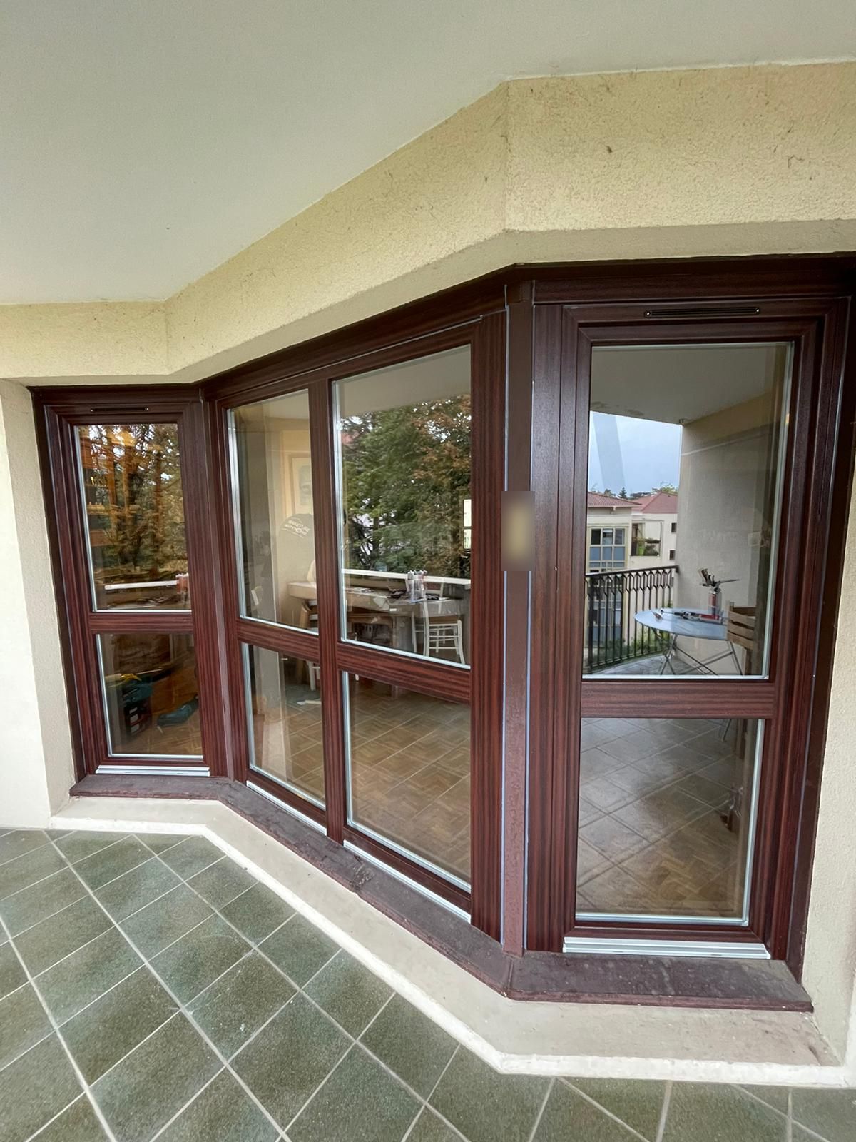 Fenêtres et porte-fenêtre en angle ton acajou formant un bow-window sur une loggia carrelée