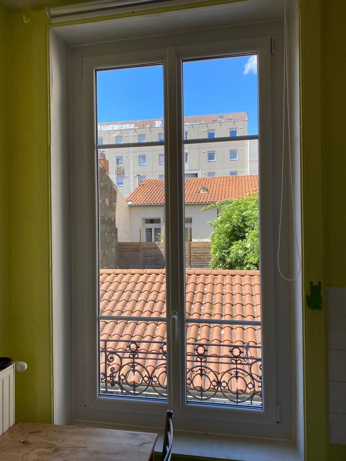 Fenêtre blanche à deux vantaux dans un appartement ancien, avec vue sur les toits de tuiles et un garde-corps en fer forgé
