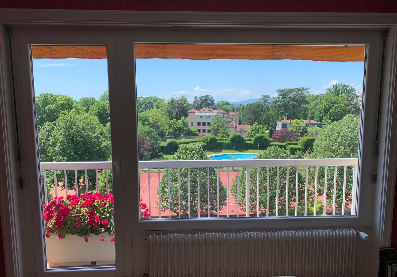 Ensemble porte-fenêtre et grande fenêtre blanches sur un balcon fleuri, vue sur un parc arboré