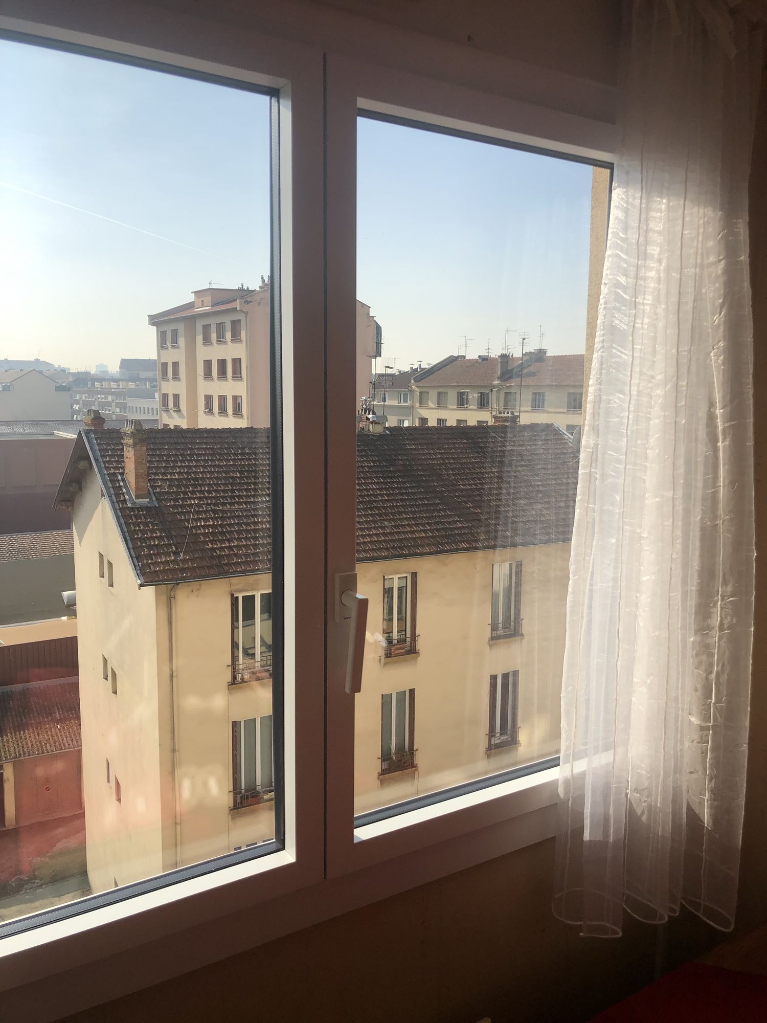 Fenêtre aluminium à deux vantaux, vue sur les toits d'un quartier ancien