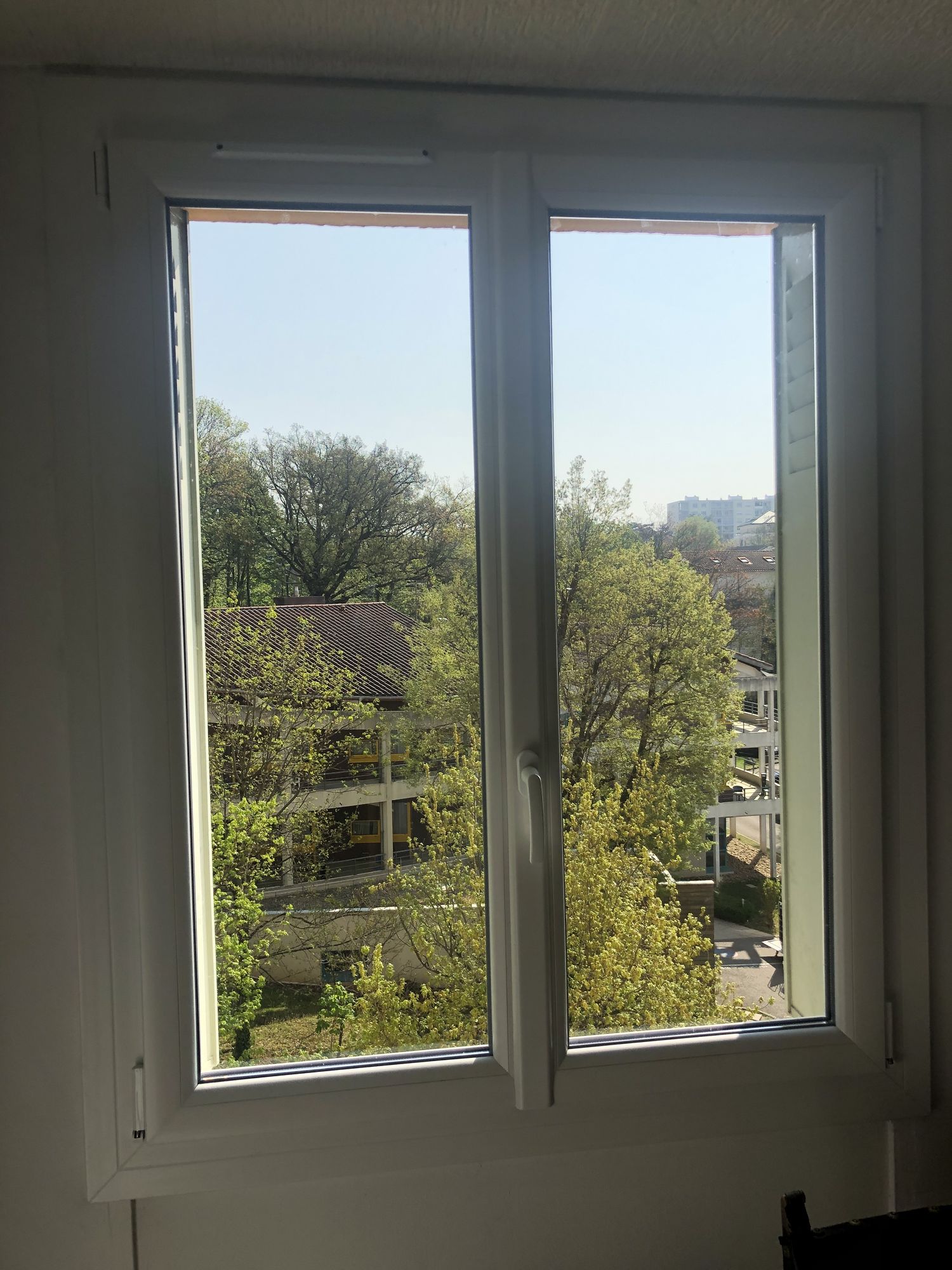 Fenêtre PVC blanche à deux vantaux ouvrant sur des arbres, vue depuis l'intérieur