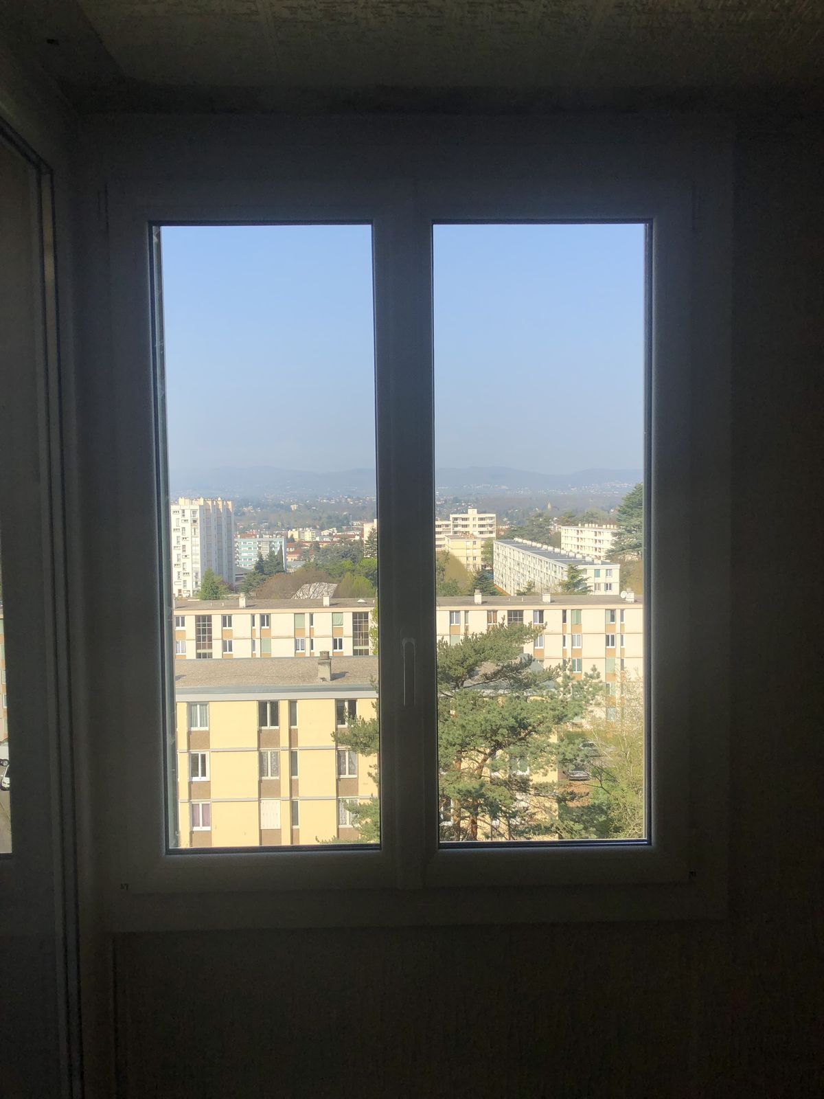 Fenêtre PVC blanche à deux vantaux en étage, avec vue sur la ville