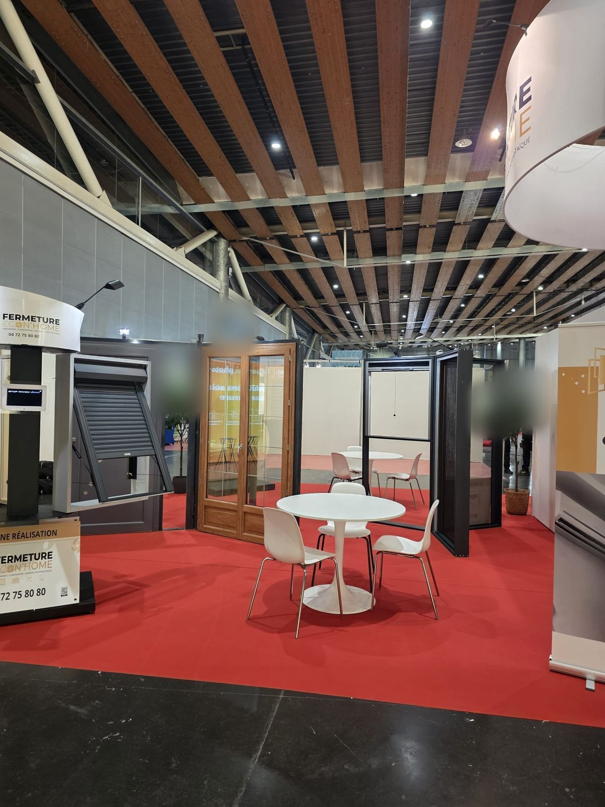 Vue du stand au Lille Grand Palais : fenêtre avec volet roulant, porte-fenêtre ton bois et coin accueil sous l'enseigne ronde Fermeture Econ'Home