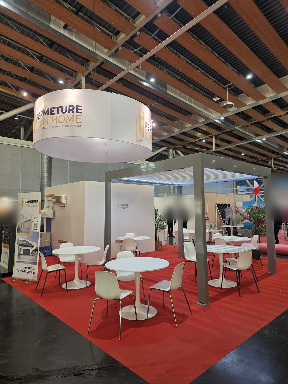 Pergola en aluminium abritant des tables et chaises blanches sur le stand, avec un kakémono fenêtres, volets et stores