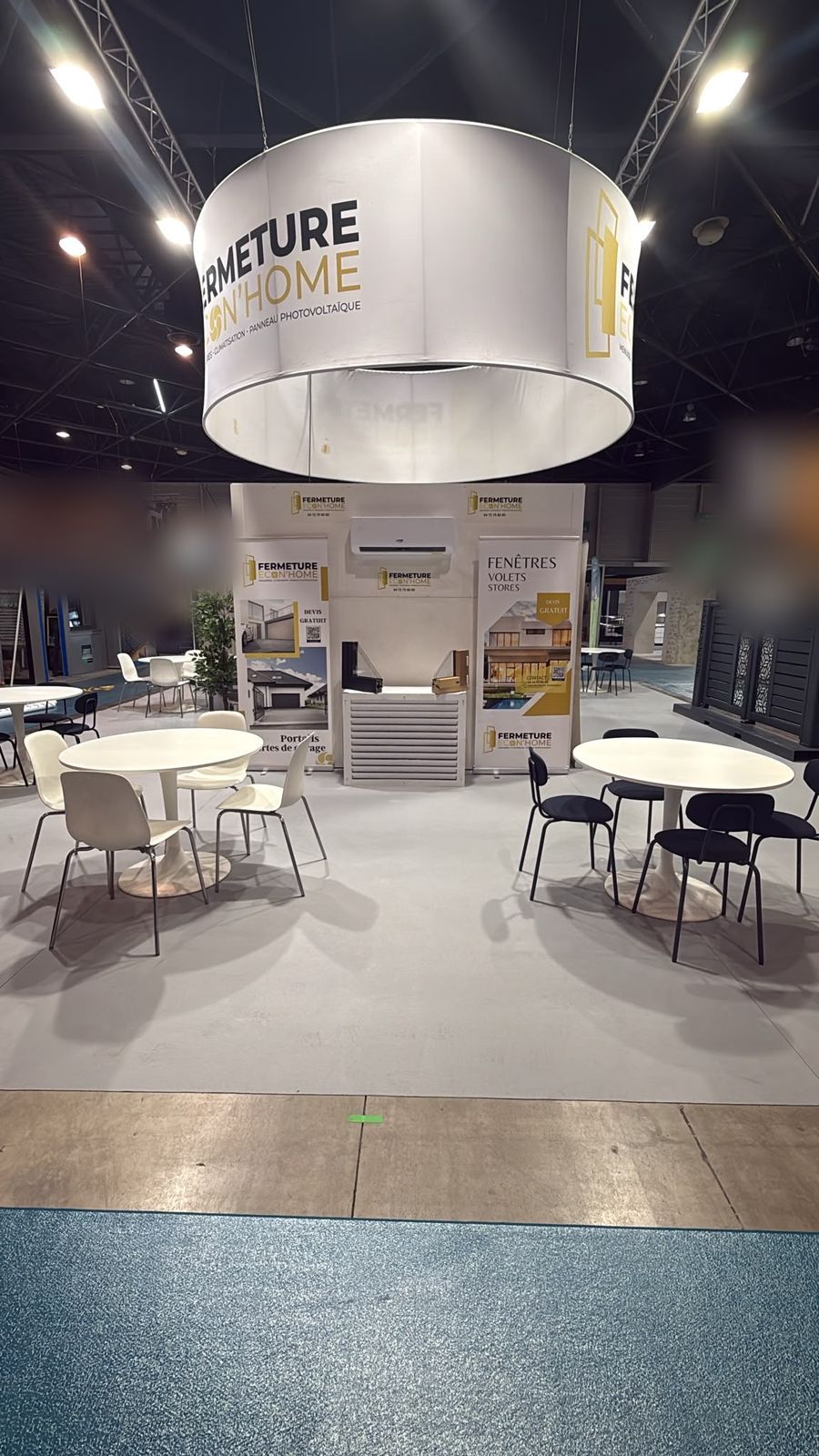 Coin salon du stand au Parc Chanot avec tables rondes et chaises, sous l'enseigne ronde Fermeture Econ'Home