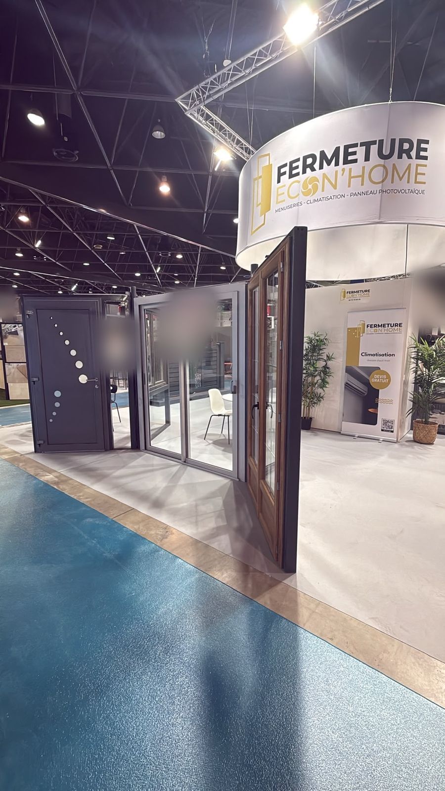 Porte d'entrée grise à hublots et porte-fenêtre ton bois ouverte, exposées sur le stand