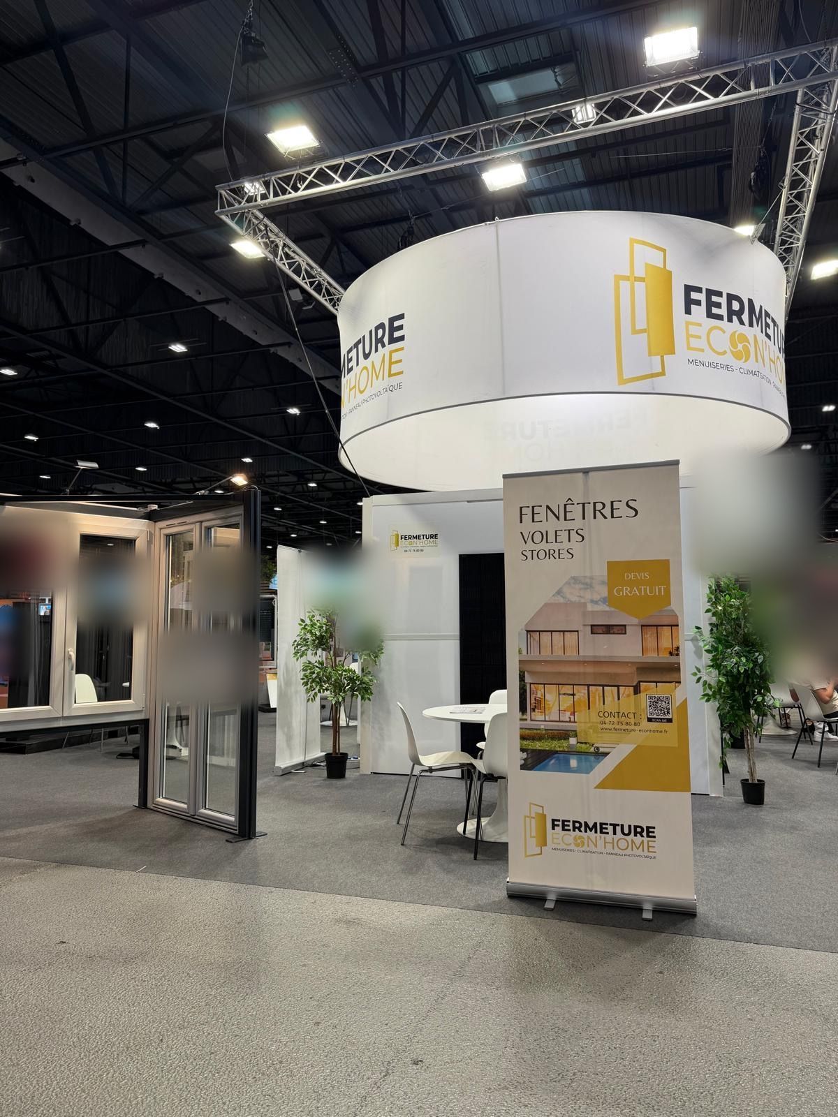 Vue d'ensemble du stand au Parc Expo de Saint-Étienne : porte-fenêtre, kakémono fenêtres, volets et stores, coin salon sous l'enseigne ronde