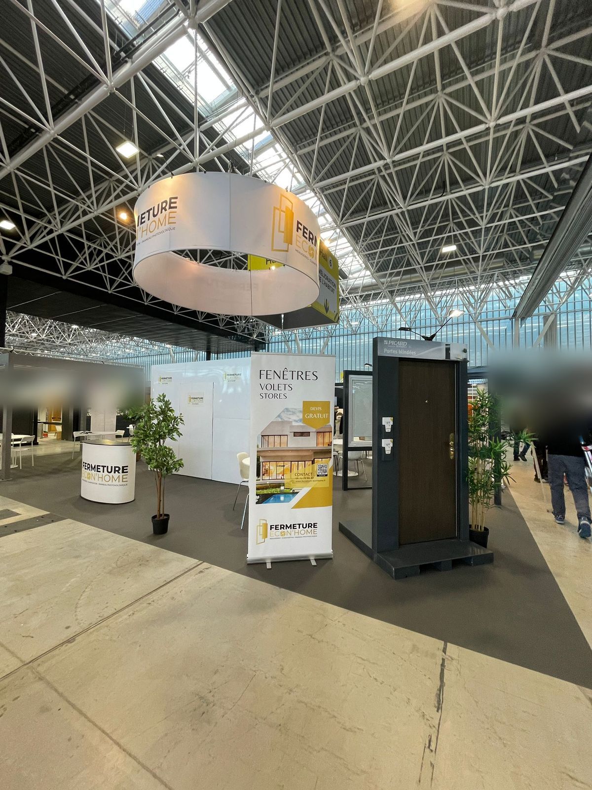 Porte d'entrée grise et kakémono fenêtres, volets et stores sur le stand, sous l'enseigne ronde Fermeture Econ'Home
