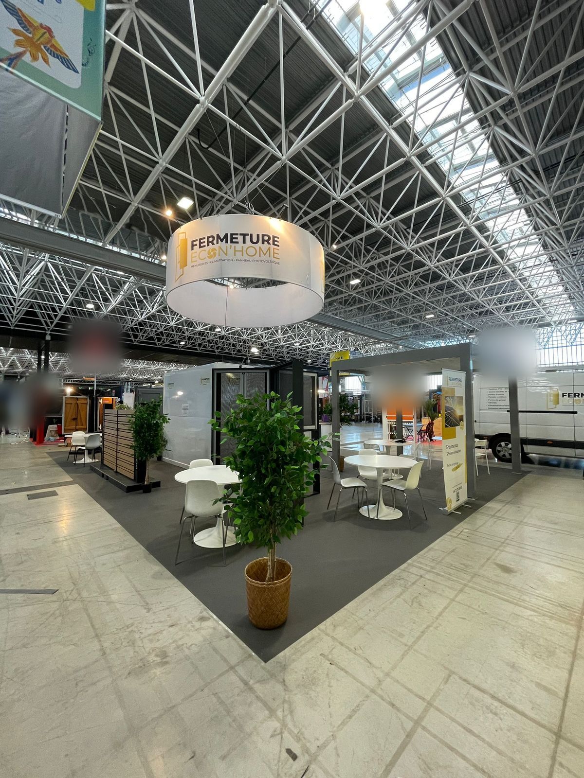 Vue du stand depuis l'allée : coin salon, plante verte et produits exposés sous l'enseigne ronde