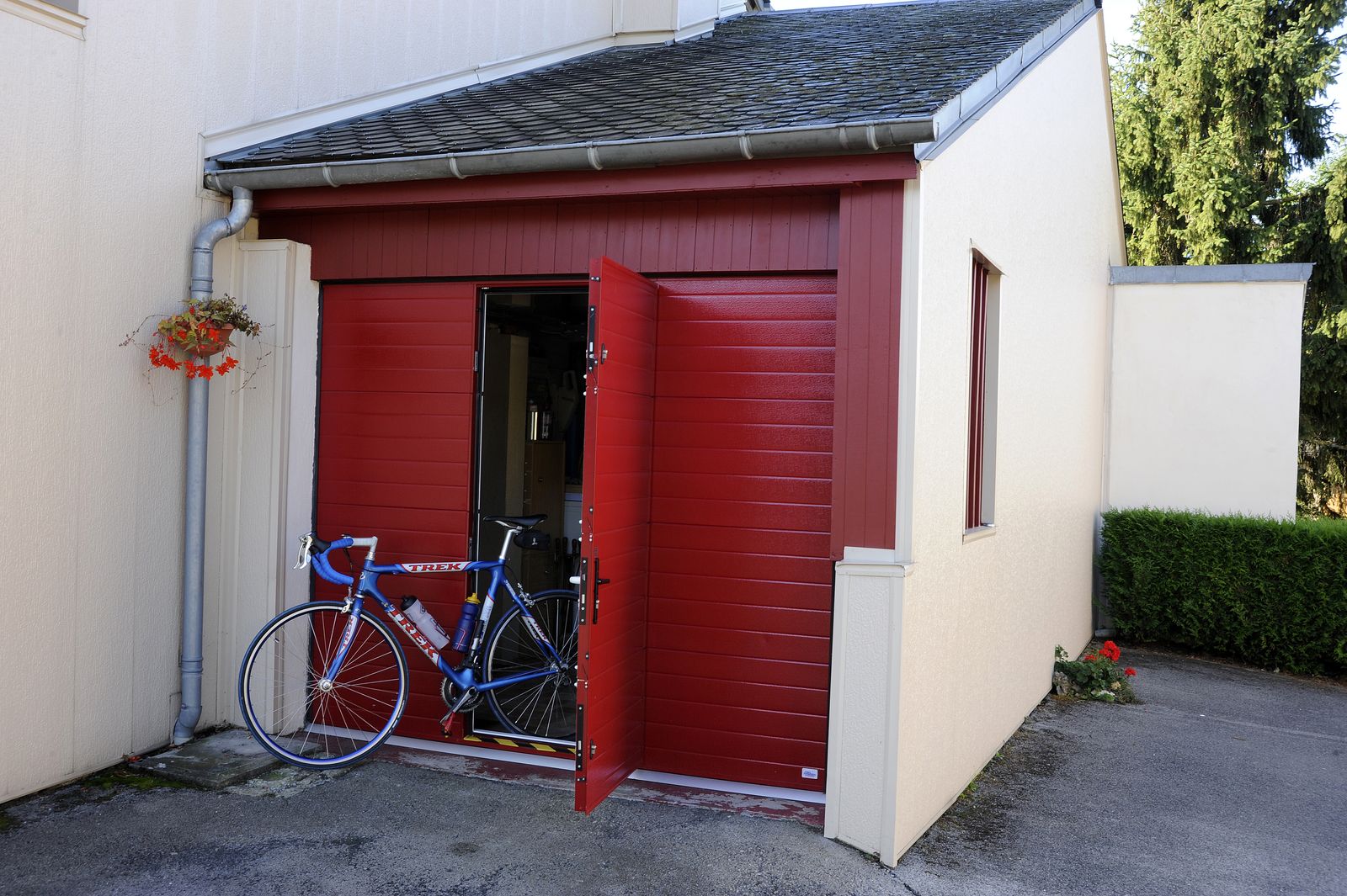 Porte de garage sectionnelle rouge à rainures horizontales dont le portillon intégré est ouvert, un vélo appuyé devant