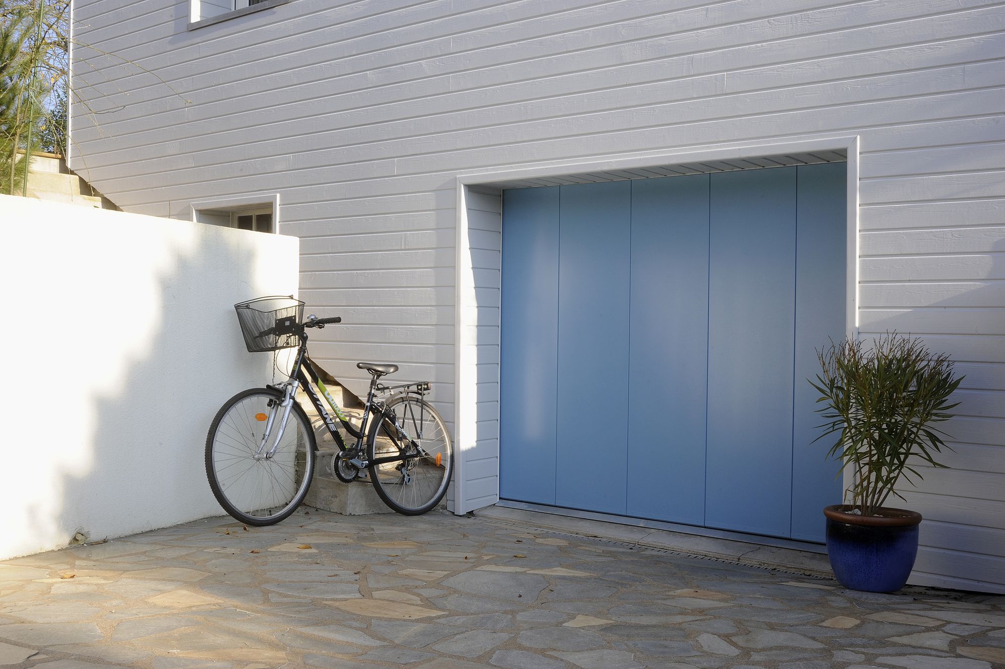 Porte de garage latérale à panneaux lisses verticaux bleu pastel sur une maison à bardage blanc