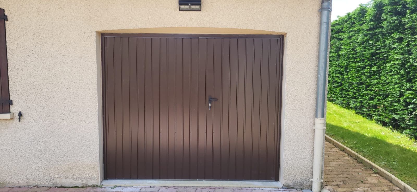 Porte de garage basculante brune à rainures verticales sur une façade claire