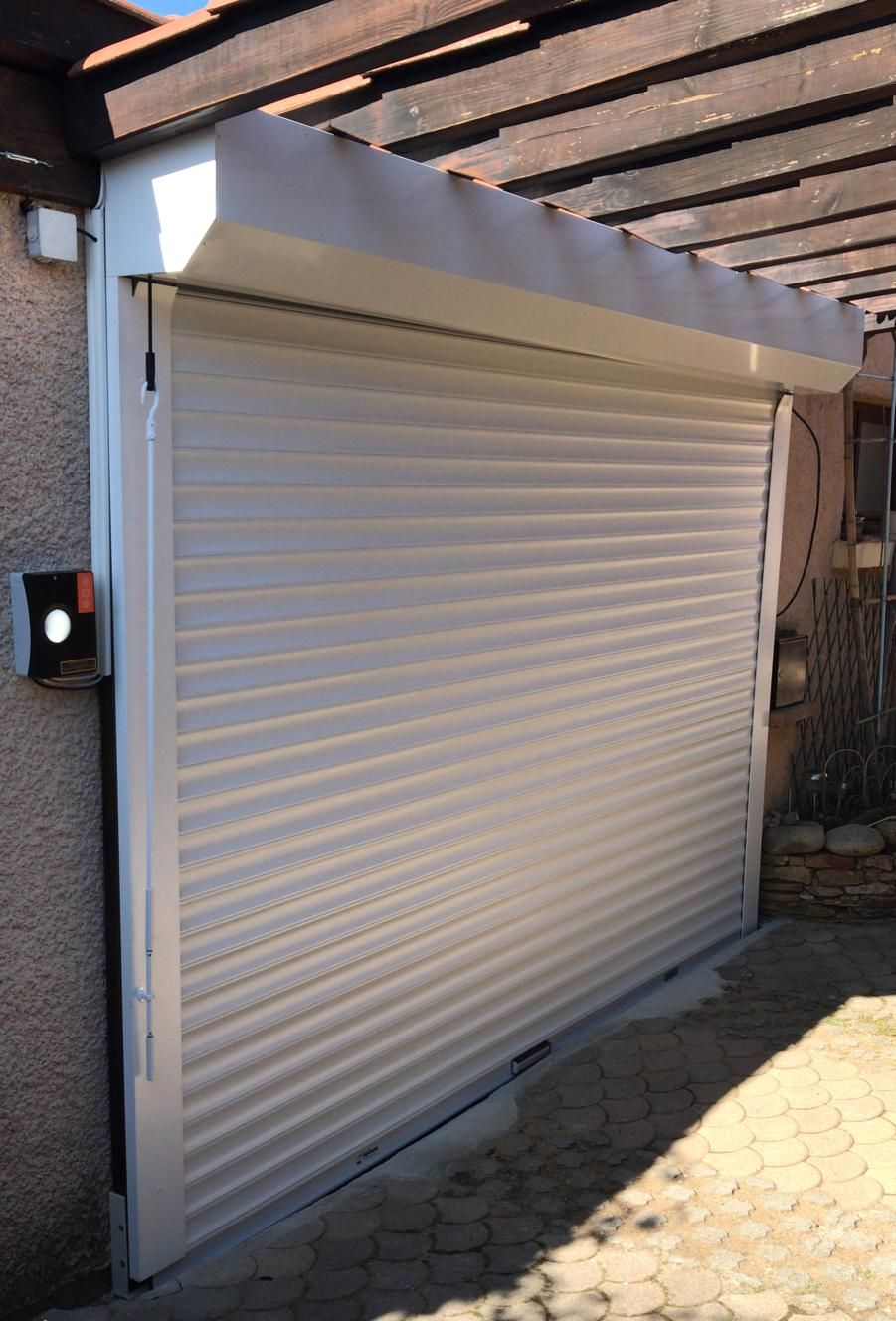 Porte de garage enroulable blanche avec son coffre, sous une pergola en bois