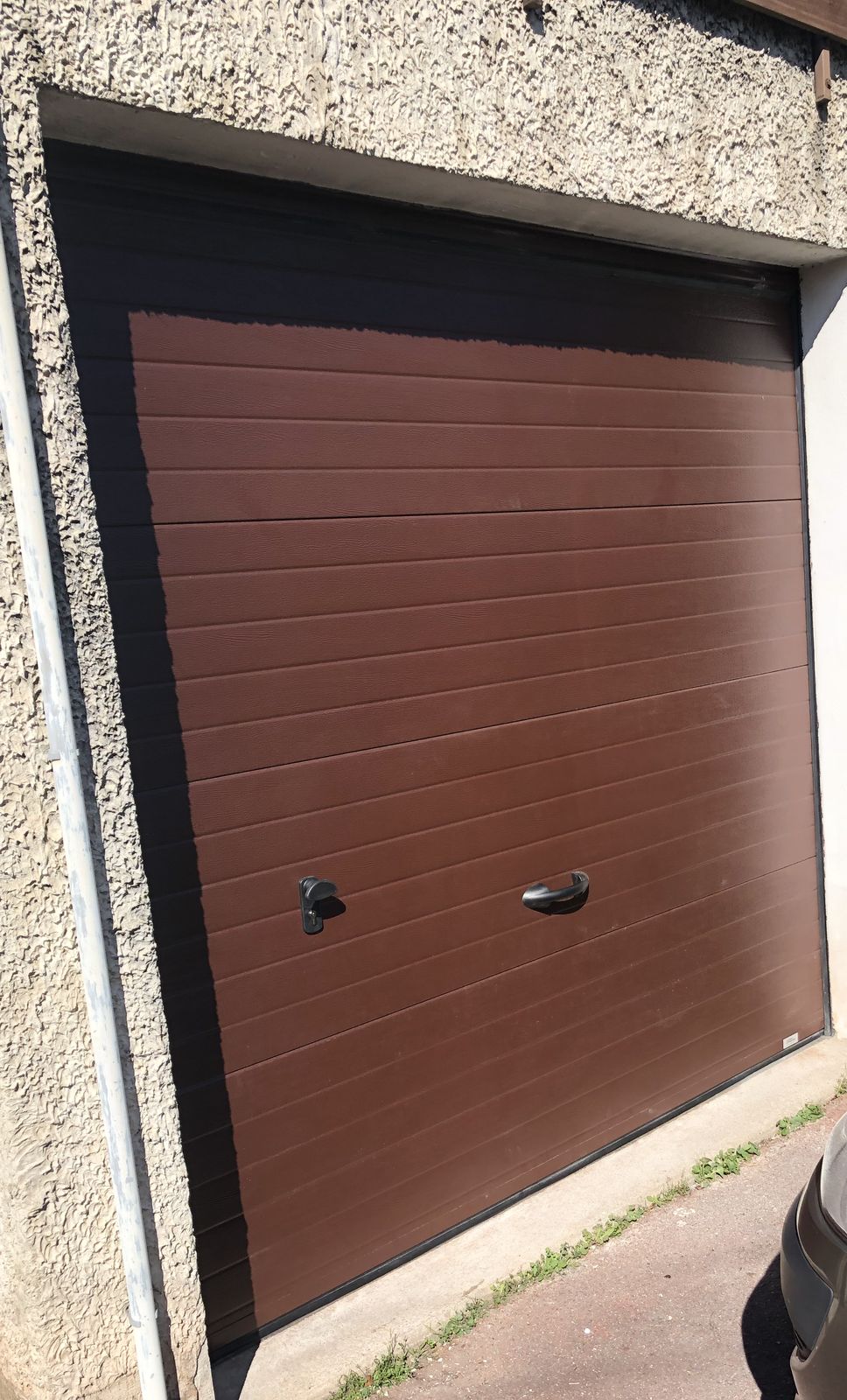 Porte de garage sectionnelle brune à rainures horizontales posée dans une maison