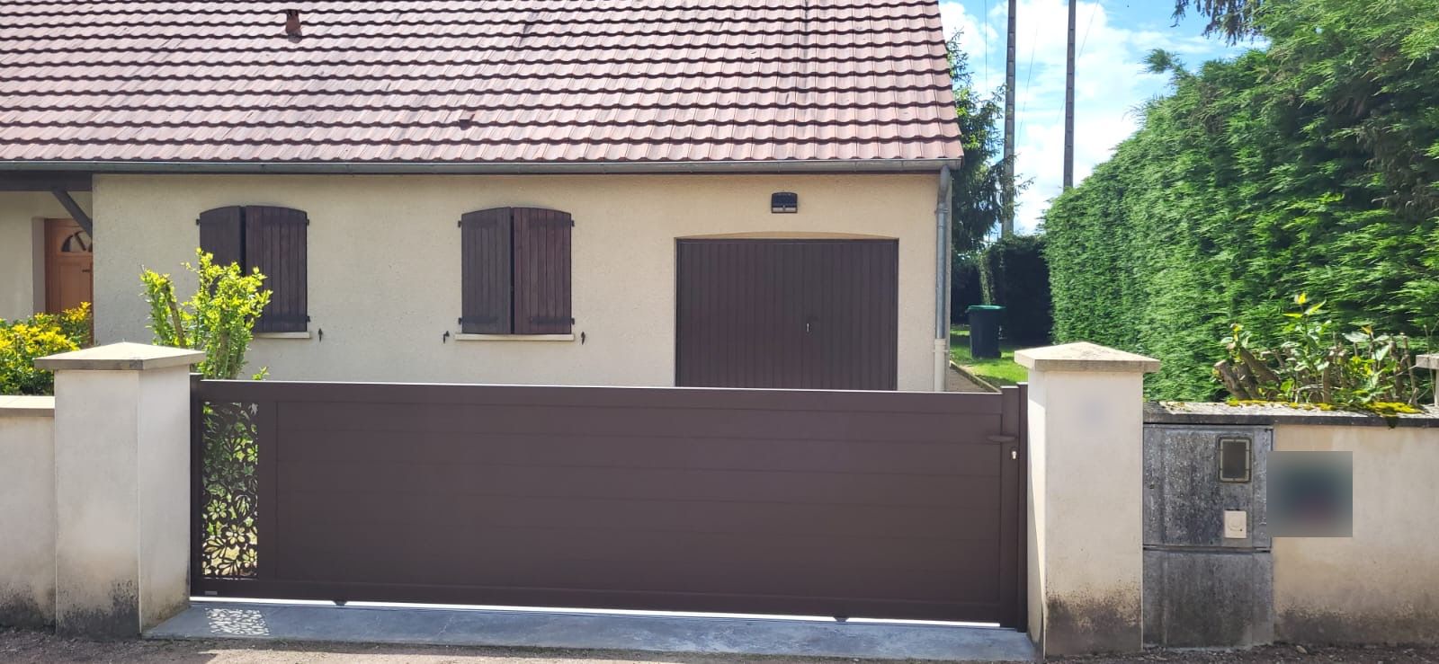 Portail coulissant aluminium brun avec panneau décoratif ajouré, devant une maison