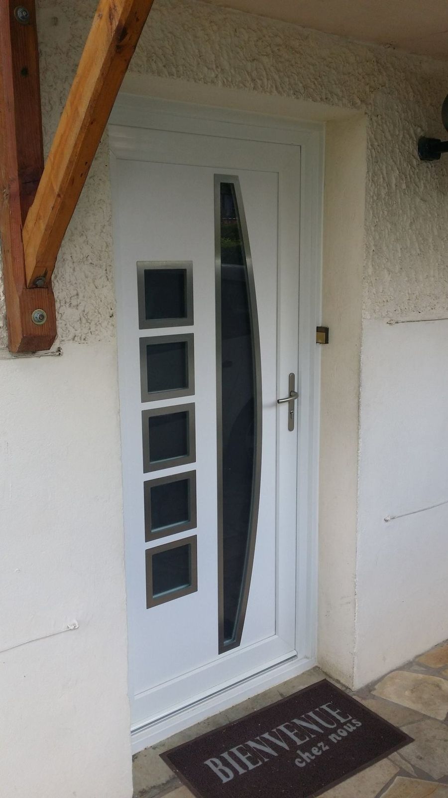 Porte d'entrée blanche contemporaine avec hublots carrés et long vitrage courbe, sous un auvent en bois
