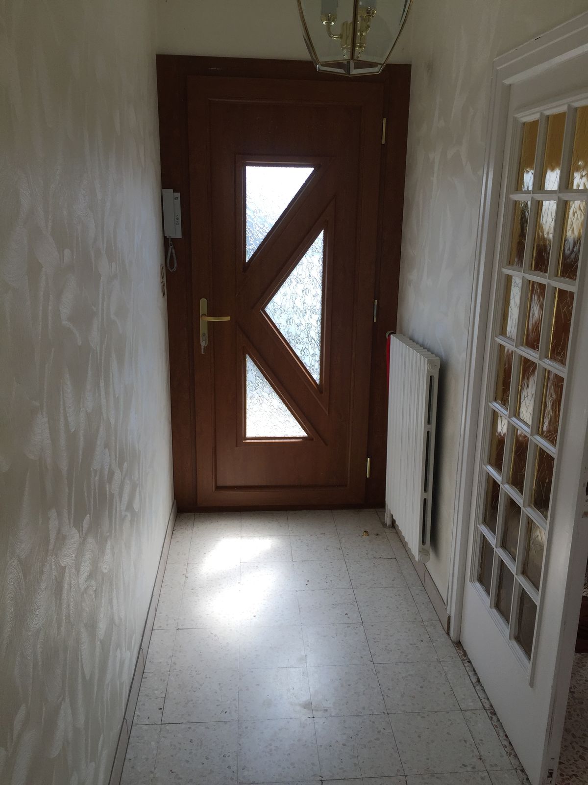 Porte d'entrée ton bois à vitrages triangulaires vue de l'intérieur, au bout d'un couloir