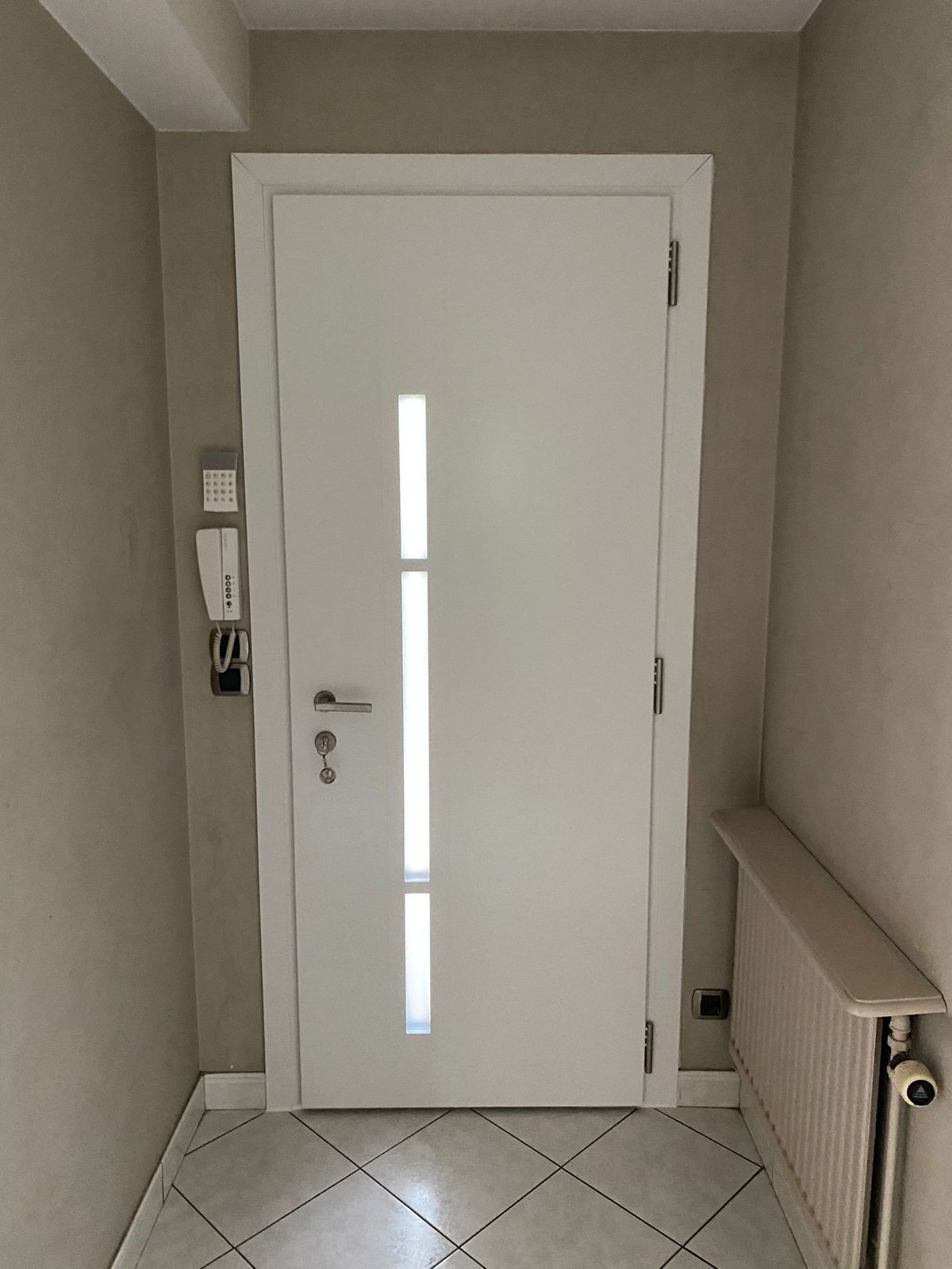 Porte d'entrée blanche à trois inserts vitrés verticaux, vue depuis un hall d'entrée carrelé
