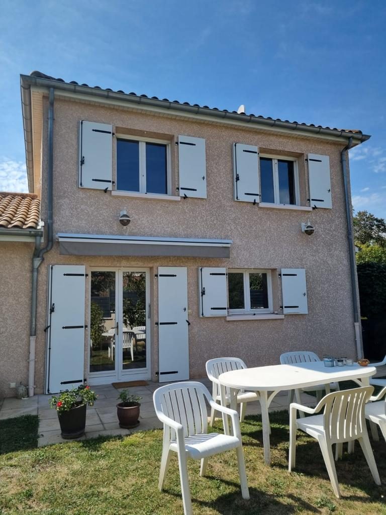 Maison crépie avec fenêtres, porte-fenêtre et volets battants blancs, devant une pelouse avec salon de jardin