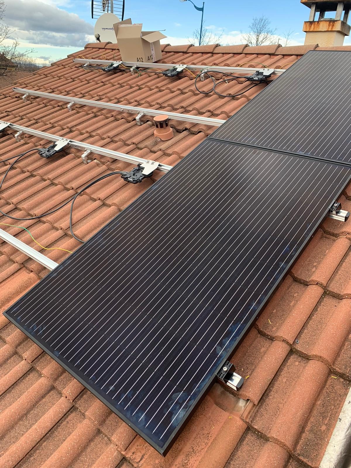 Panneaux photovoltaïques noirs en cours de pose sur leurs rails, sur un toit en tuiles