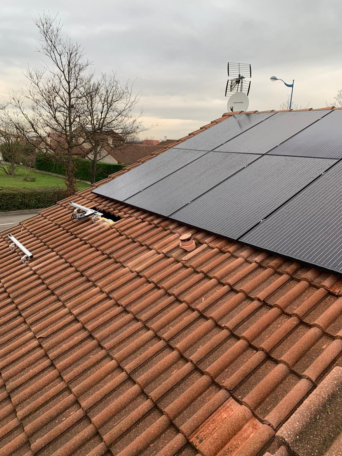 Panneaux photovoltaïques noirs posés sur le toit en tuiles rouges d'une maison individuelle