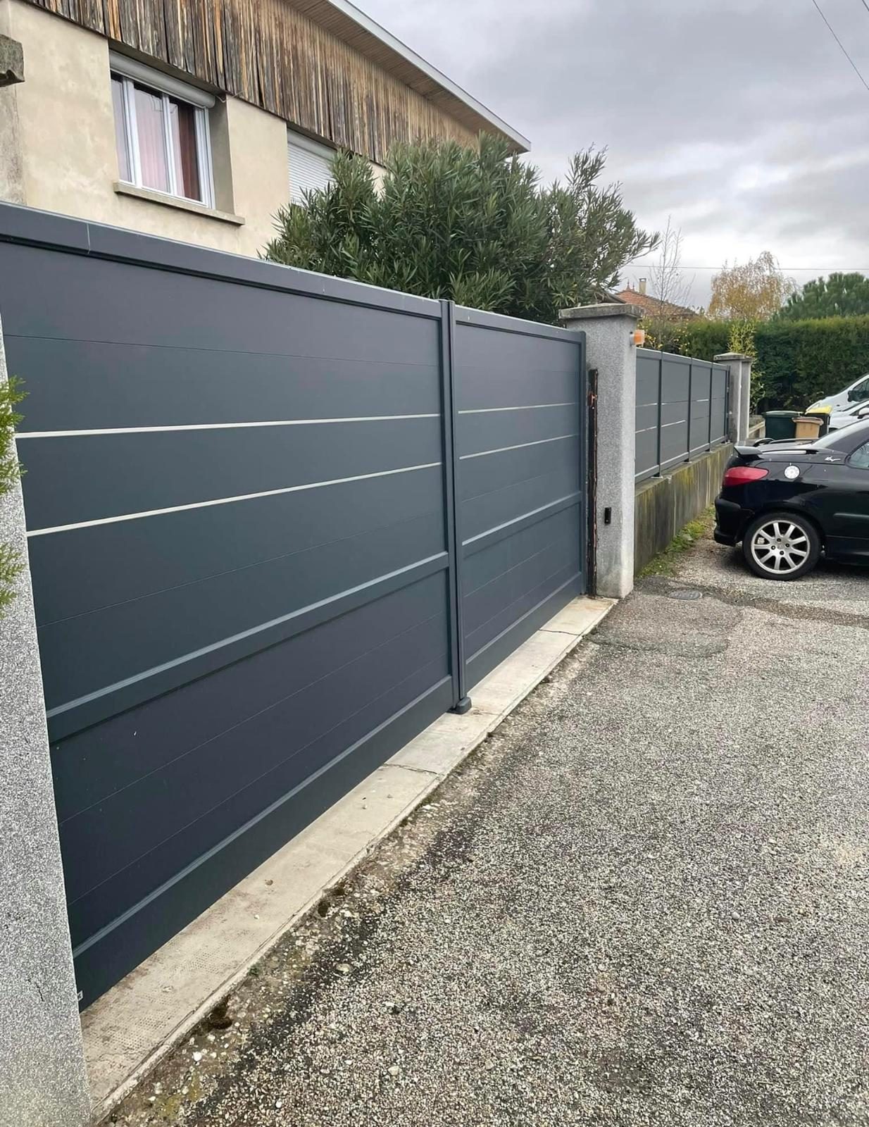 Portail aluminium gris anthracite à lames horizontales et clôture assortie posée sur un muret, le long d'une allée