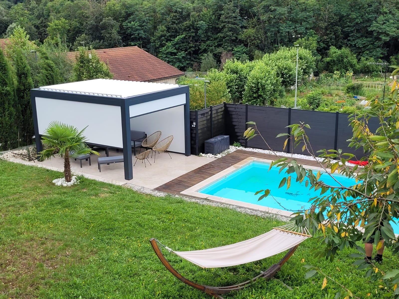 Pergola gris anthracite et blanc au fond d'un jardin, au bord d'une piscine
