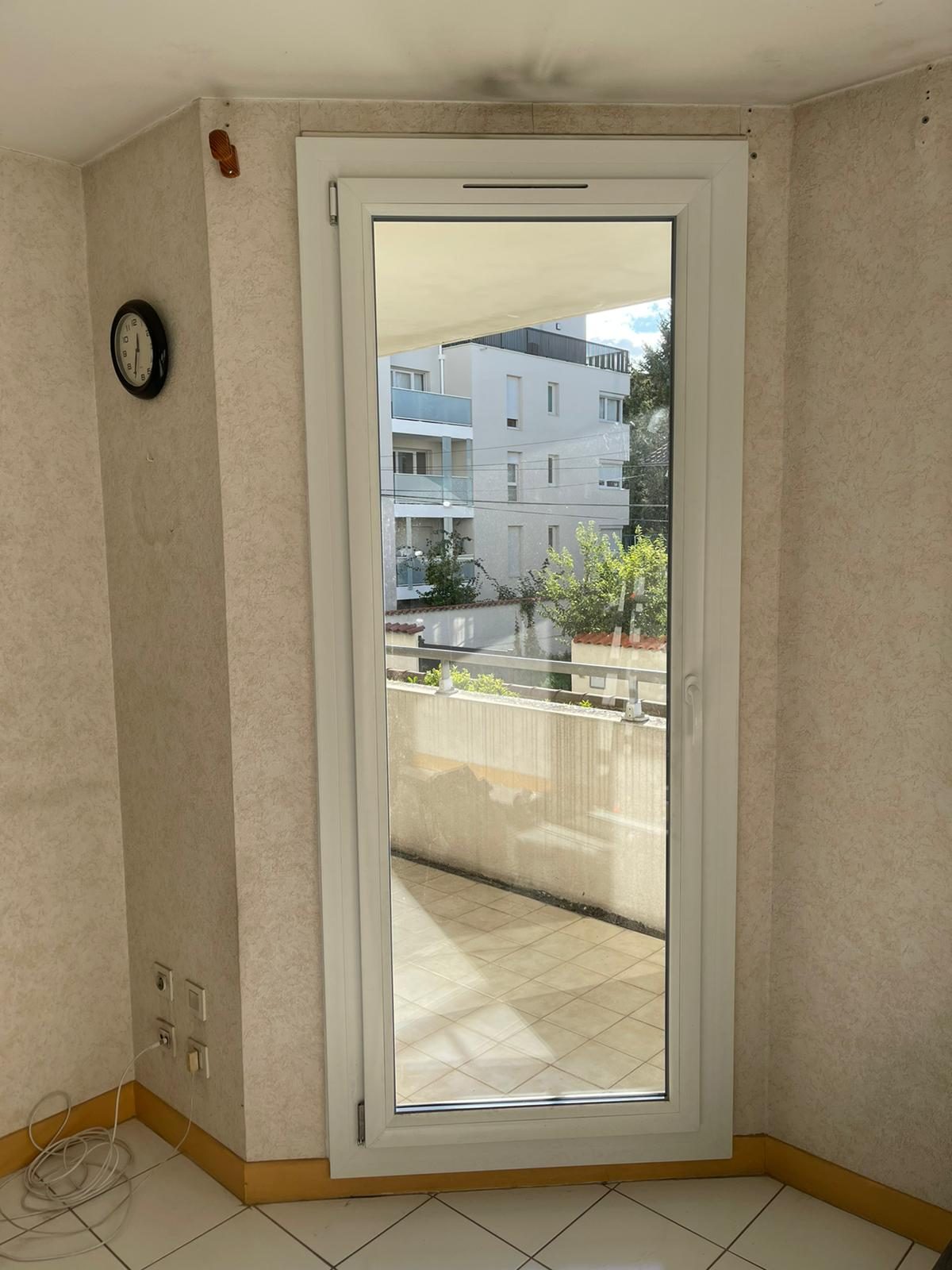 Porte-fenêtre blanche à un vantail donnant sur une terrasse carrelée d'appartement