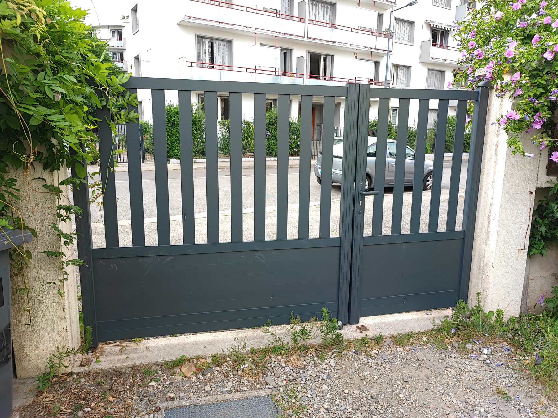 Portail battant deux vantaux gris anthracite à barreaux et soubassement plein, à l'entrée d'une résidence