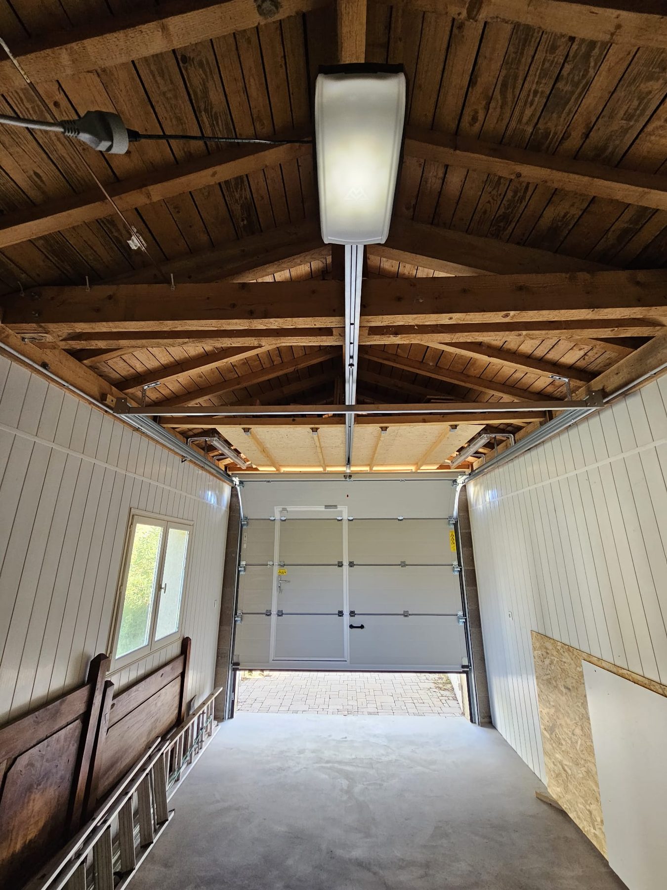 Porte de garage sectionnelle blanche vue de l'intérieur d'un garage à charpente en bois