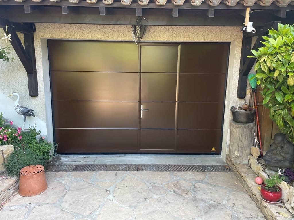 Porte de garage brune avec portillon intégré, sous une avancée de toit en bois