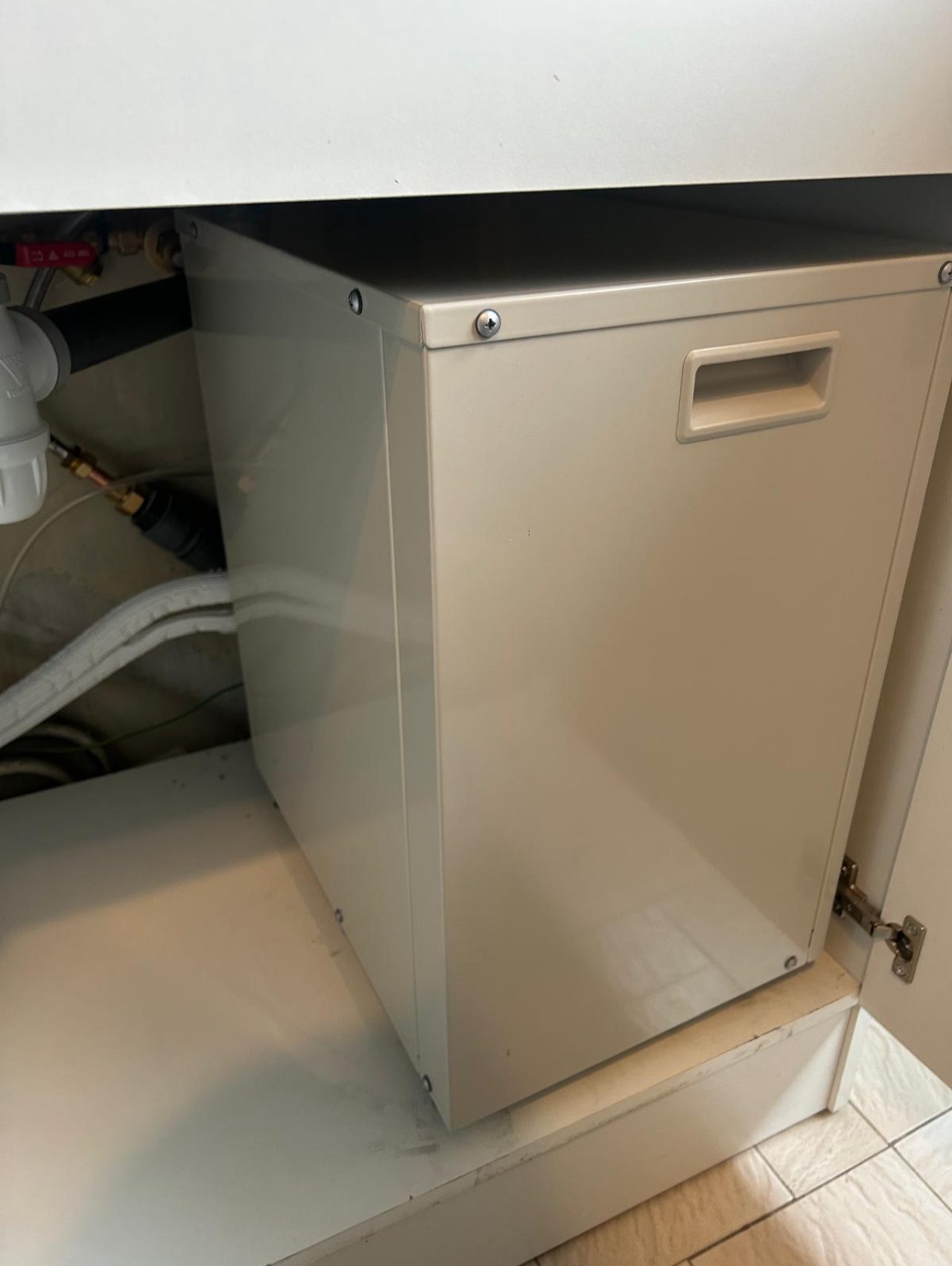 Caisson d’une unité de climatisation compacte logé dans un meuble sous évier, à côté de ses gaines de raccordement