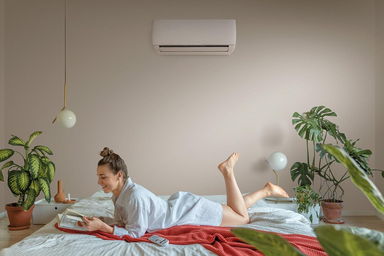 Chambre rafraîchie par un climatiseur mural, une femme lisant allongée sur le lit
