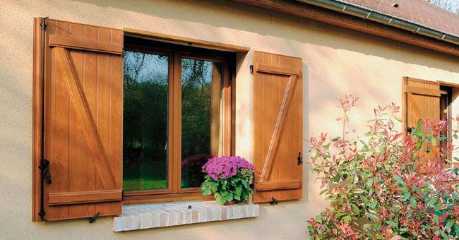 Volets battants en bois ton naturel, à barres et écharpe, ouverts de part et d'autre d'une fenêtre fleurie