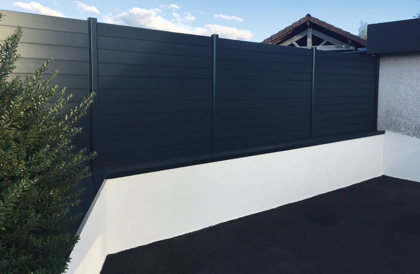 Clôture aluminium gris anthracite à lames pleines posée sur un muret blanc