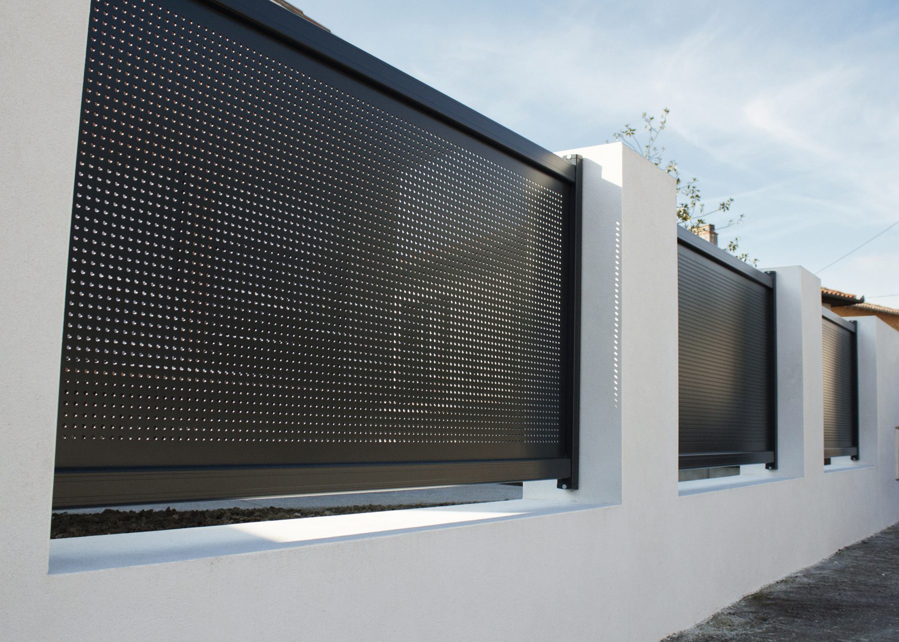 Clôture à panneaux aluminium perforés gris anthracite entre des piliers maçonnés blancs