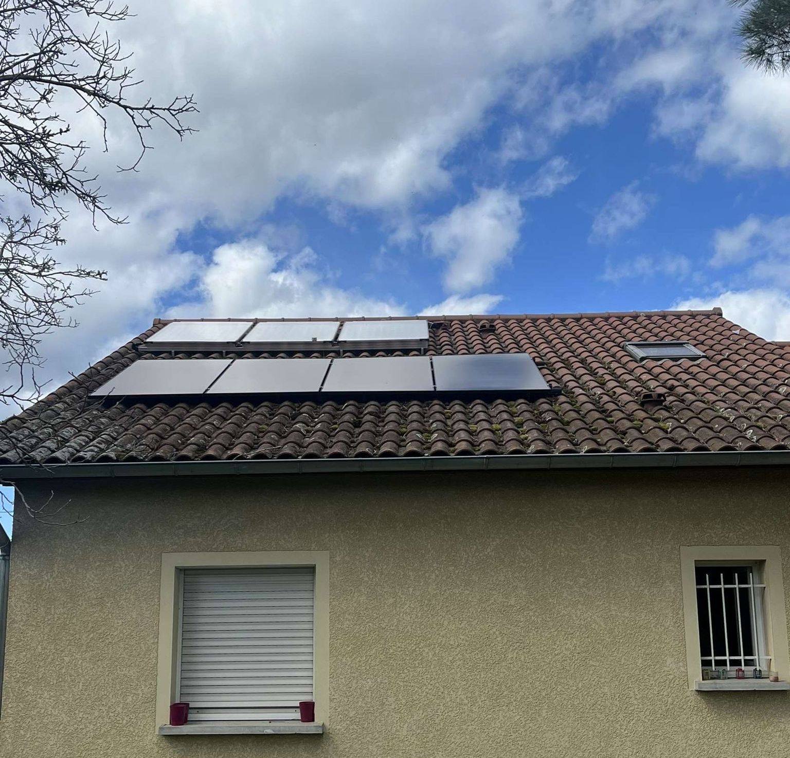 Maison individuelle avec des panneaux solaires sur son toit en tuiles, sous un ciel bleu nuageux
