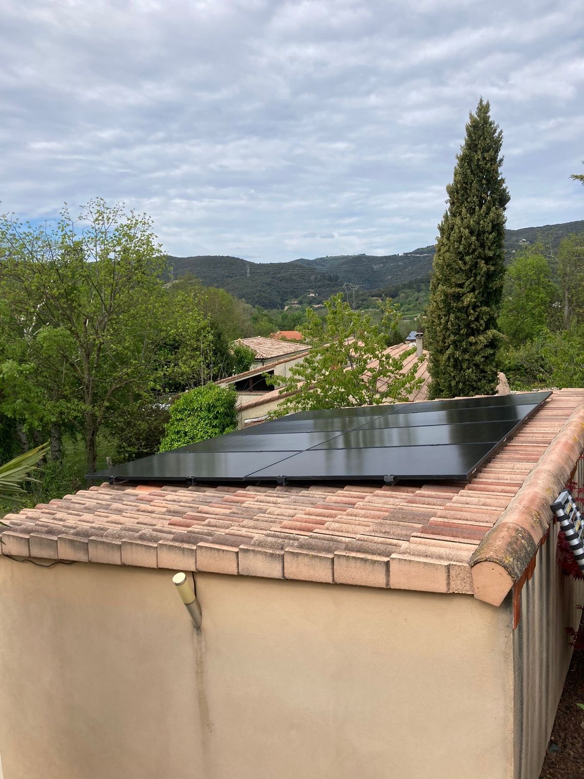 Panneaux photovoltaïques noirs sur le toit en tuiles d'une annexe, devant des collines boisées